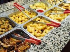 Et buffetbord med forskellige stegte fødevarer, herunder pommes frites, løgringe, mishandlede genstande og ribben, med hver ret i en metalbakke og serveringstænger placeret i bakkerne.
