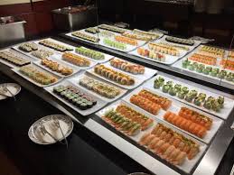 En buffet-udstilling viser flere fade med sushi-varianter arrangeret pænt på en disk med tomme tallerkener og serveringsredskaber i forgrunden.
