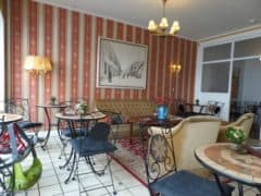Et hyggeligt caféinteriør med en blanding af smedejern og polstrede siddepladser, mønstret tapet, et stort indrammet billede og flere små borde med blomsterarrangementer.