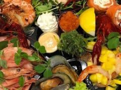 En fiske- og skaldyrstallerken med rejer, muslinger, languster, røget laks, rød kaviar, forskellige saucer, citronbåde, blandet grønt og mango i tern.