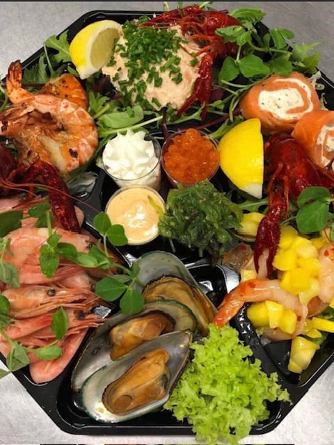 En fiske- og skaldyrstallerken med rejer, muslinger, languster, røget laks, rød kaviar, forskellige saucer, citronbåde, blandet grønt og mango i tern.