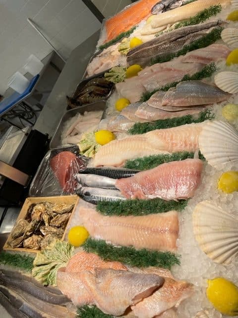 En udstilling af friske skaldyr på is, herunder forskellige fiskefileter, hele fisk, østers og kammuslinger, garneret med persille og citronhalvdele.