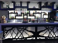 En moderne bar med et geometrisk, sort-hvidt design, forskellige flasker alkohol på oplyste hylder, glasvarer og eklektiske dekorationer, inklusive en Maneki-neko kattestatue.