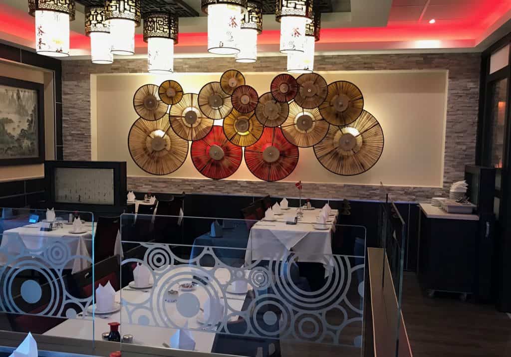 En tom restaurant med cirkulære vægdekorationer og hvide duge på dækkede borde. Loftslys er tændt, og vægge har grå og røde accenter.
