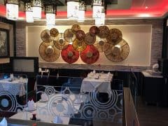 En tom restaurant med cirkulære vægdekorationer og hvide duge på dækkede borde. Loftslys er tændt, og vægge har grå og røde accenter.