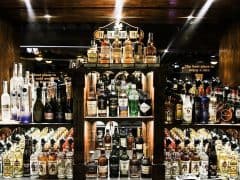 En velassorteret bar med et udvalg af spiritusflasker, herunder whisky, vodka og vin, arrangeret på hylderne. Skiltning over og omkring baren fremhæver etablissementets indbydende atmosfære.