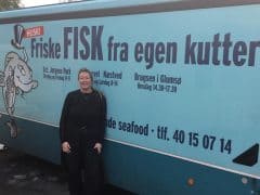 Byliv.nu: En person, der står foran en blå fiskebil med teksten "Friske FISK fra egen kutter.