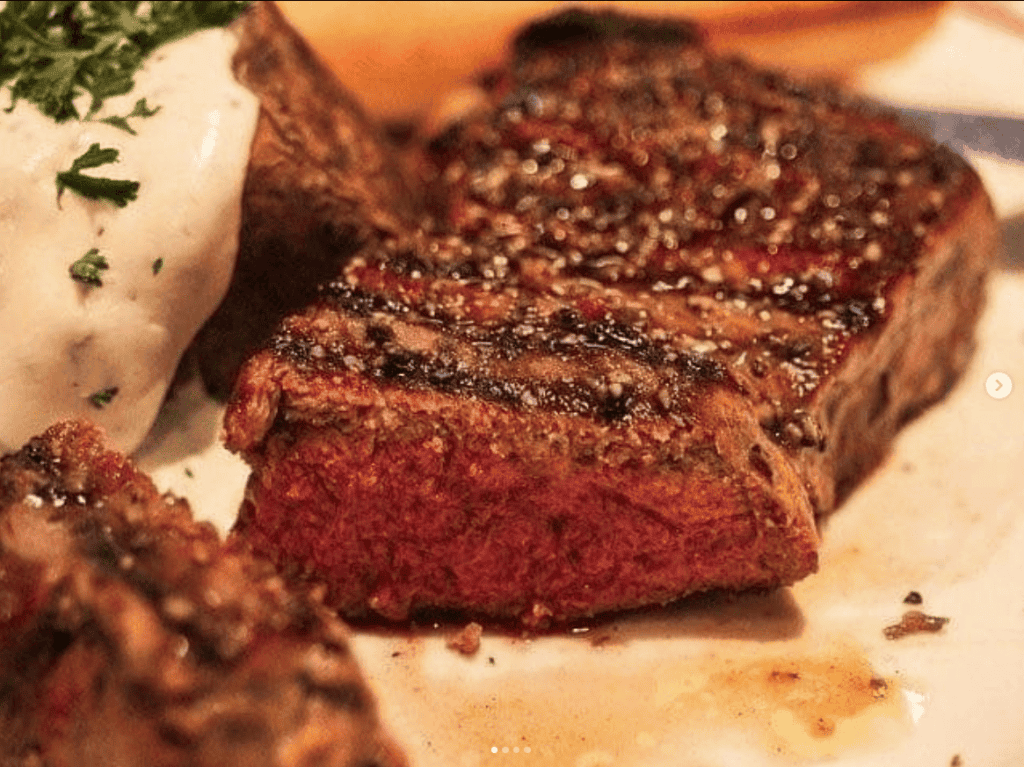Byliv.nu: Nærbillede af en grillet bøf med rødt indre, serveret med en bagt kartoffel toppet med en klat creme fraiche og garneret med persille.