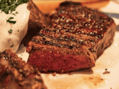 Byliv.nu: Nærbillede af en grillet bøf med rødt indre, serveret med en bagt kartoffel toppet med en klat creme fraiche og garneret med persille.