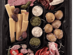 Byliv.nu: En sort bakke med sektioner indeholdende diverse oste, speget kød, fyldte peberfrugter, oliven, pickles, soltørrede tomater, pesto og dipsauce.