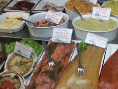 Byliv.nu: Et udvalg af fisk og skaldyr, smørepålæg og garnerede retter vist i en delikatessekasse, mærket med små skilte på et andet sprog end engelsk.