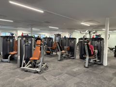 Byliv.nu: Folk, der bruger træningsmaskiner i et fitnesscenter med nummereret udstyr og overheadbelysning.